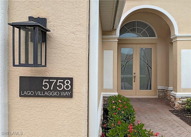 entrance to property featuring french doors, stone siding, and stucco siding