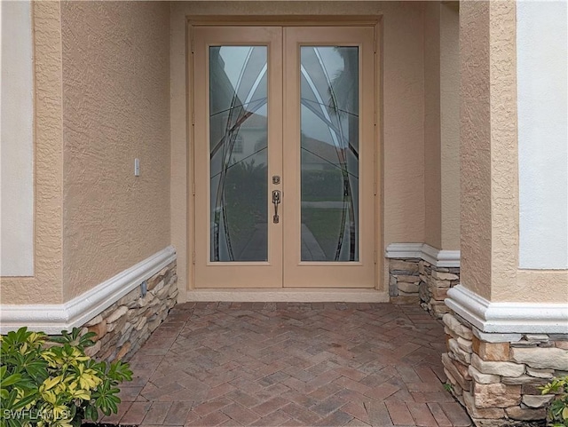 property entrance featuring french doors, stone siding, and stucco siding