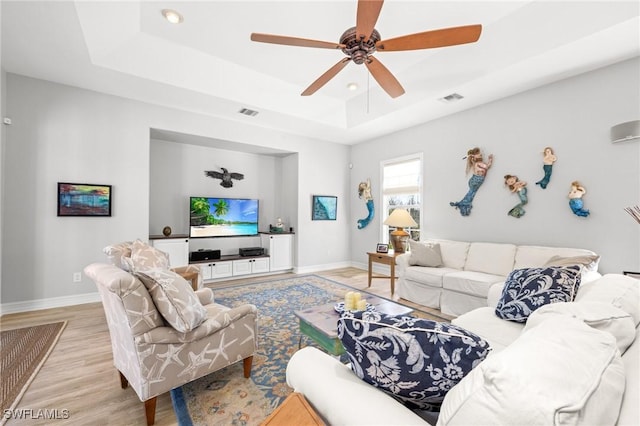 living room featuring ceiling fan, light wood-type flooring, and a tray ceiling