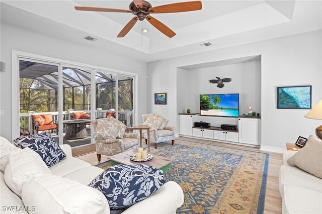 living room with light wood-type flooring, a tray ceiling, plenty of natural light, and ceiling fan