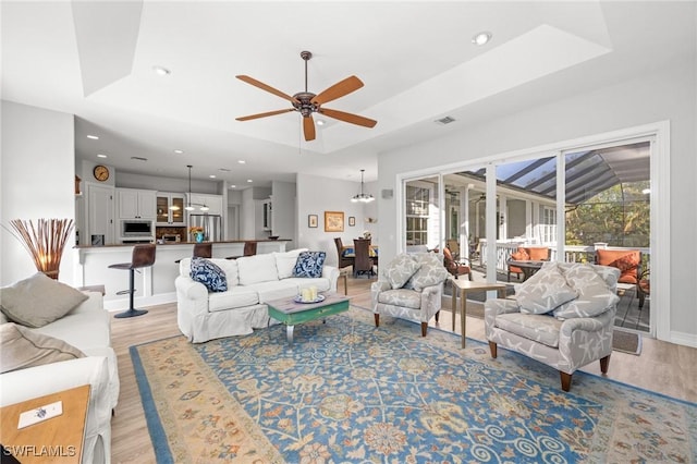 living room featuring vaulted ceiling, ceiling fan with notable chandelier, and light wood-type flooring