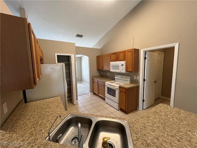 kitchen with high vaulted ceiling, sink, white appliances, and light tile patterned floors