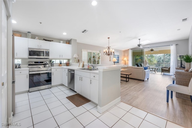 kitchen with kitchen peninsula, decorative light fixtures, stainless steel appliances, and white cabinets