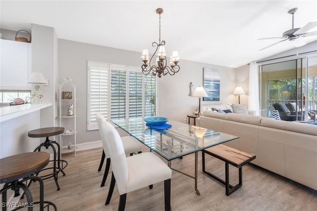 dining room with ceiling fan with notable chandelier, light hardwood / wood-style floors, a wealth of natural light, and lofted ceiling