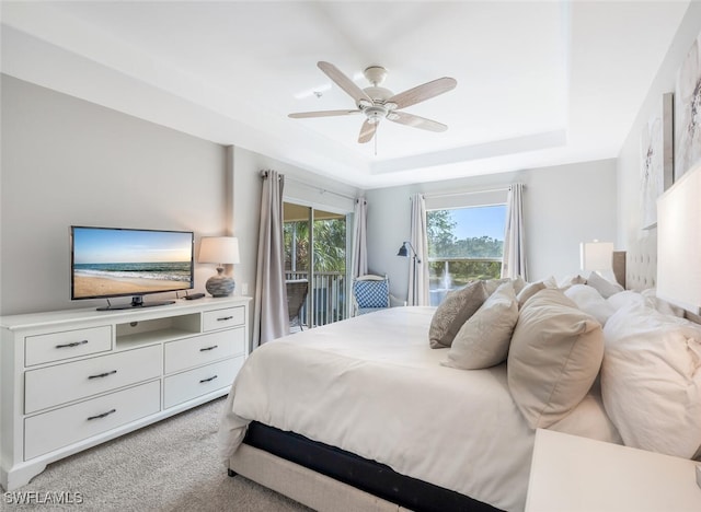 bedroom with a tray ceiling, access to exterior, ceiling fan, and light colored carpet