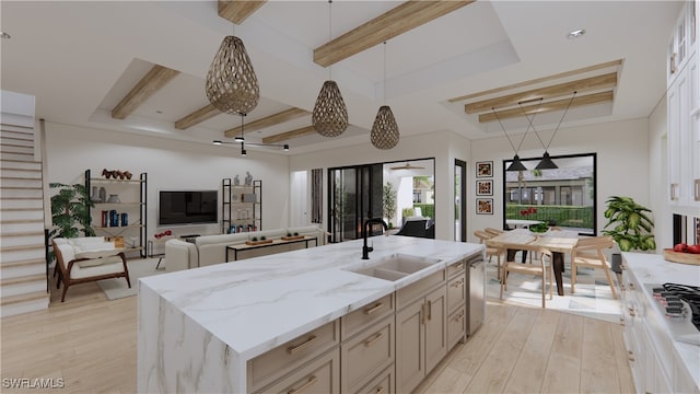 kitchen with light wood-type flooring, sink, light stone counters, and an island with sink