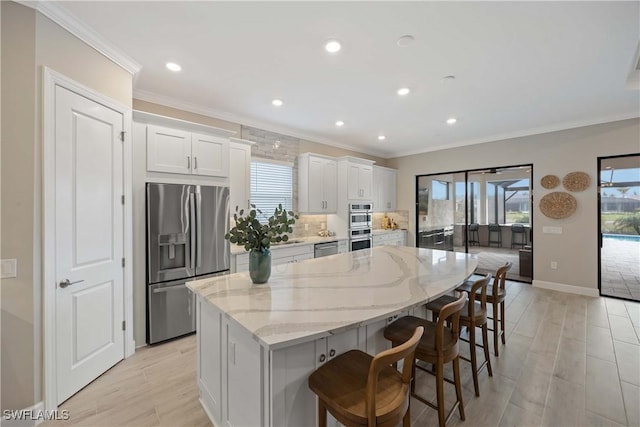 kitchen with a breakfast bar, a kitchen island, light stone counters, white cabinetry, and stainless steel appliances