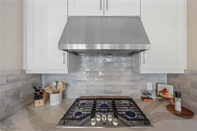 kitchen with white cabinets, wall chimney exhaust hood, light stone countertops, and backsplash