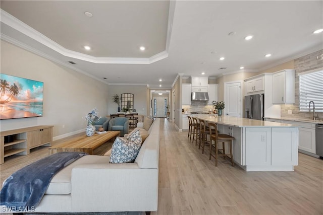 living room with a tray ceiling, sink, light hardwood / wood-style floors, and ornamental molding