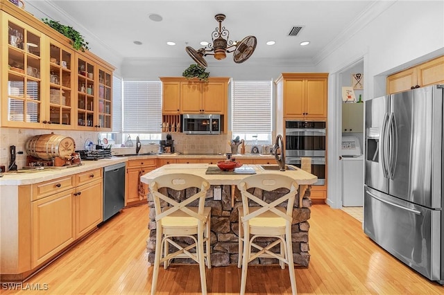 kitchen with light wood-type flooring, backsplash, ornamental molding, stainless steel appliances, and sink