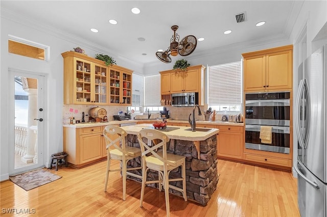 kitchen featuring decorative backsplash, appliances with stainless steel finishes, a kitchen island with sink, sink, and light hardwood / wood-style floors