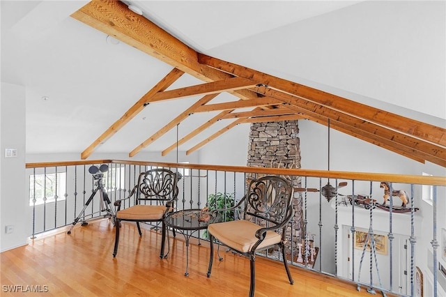 sitting room featuring hardwood / wood-style floors, vaulted ceiling with beams, and a stone fireplace