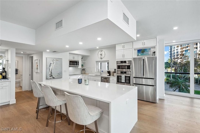 kitchen with white cabinetry, stainless steel appliances, light wood-type flooring, and a large island