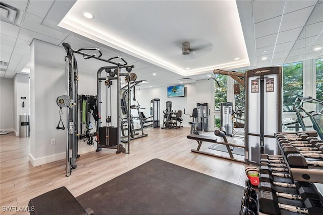 workout area featuring a raised ceiling, a wall of windows, ceiling fan, and hardwood / wood-style flooring