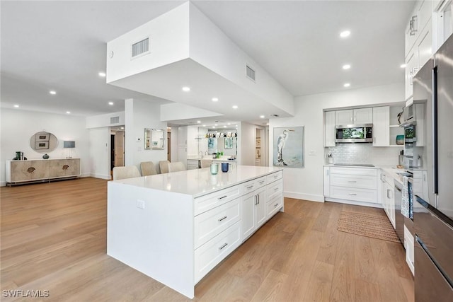 kitchen with a center island, decorative backsplash, appliances with stainless steel finishes, light hardwood / wood-style floors, and white cabinetry