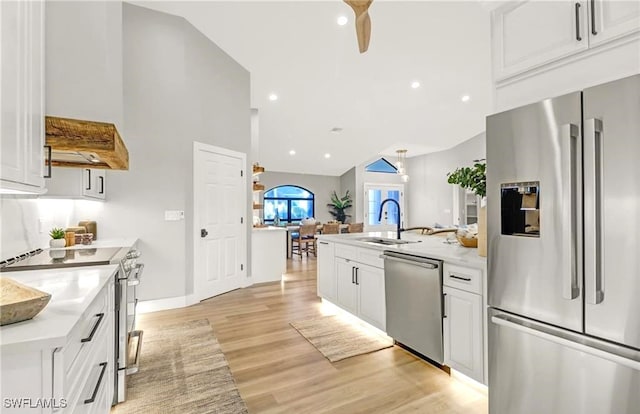 kitchen with light wood-type flooring, stainless steel appliances, vaulted ceiling, sink, and white cabinetry