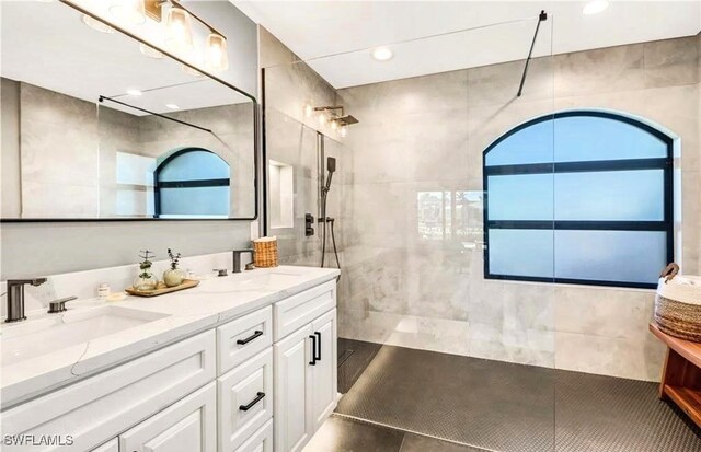 bathroom featuring tile patterned flooring, vanity, a tile shower, and tile walls