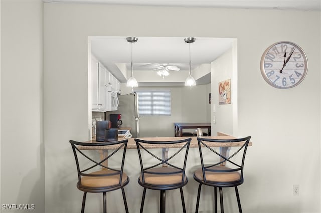 kitchen with backsplash, ceiling fan, white cabinetry, a breakfast bar area, and stainless steel refrigerator