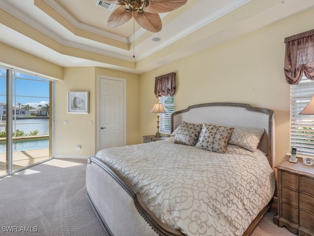 carpeted bedroom with access to outside, a water view, ceiling fan, ornamental molding, and a tray ceiling