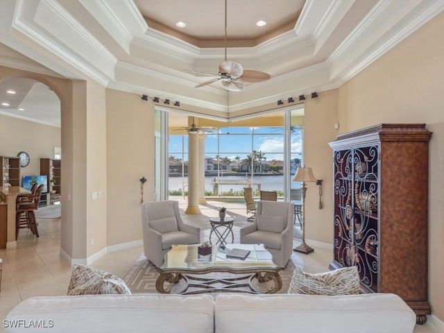 living room featuring a raised ceiling, a water view, ceiling fan, ornamental molding, and light tile patterned flooring