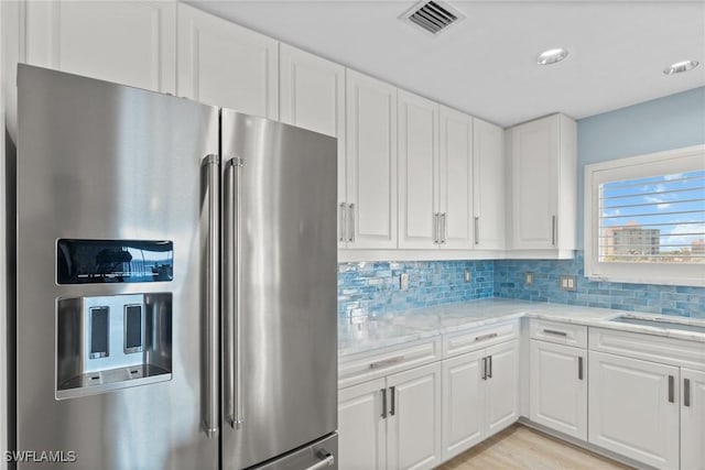 kitchen featuring decorative backsplash, stainless steel refrigerator with ice dispenser, light stone counters, sink, and white cabinets