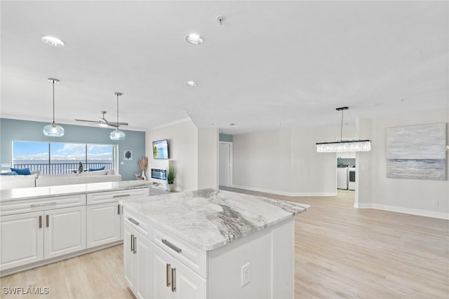 kitchen featuring washing machine and clothes dryer, ceiling fan, hanging light fixtures, a kitchen island, and white cabinets