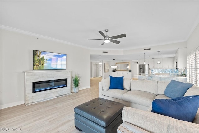 living room with ceiling fan, light hardwood / wood-style floors, ornamental molding, and a high end fireplace