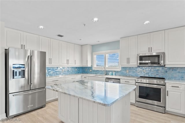 kitchen featuring white cabinetry, a center island, stainless steel appliances, light hardwood / wood-style floors, and decorative backsplash