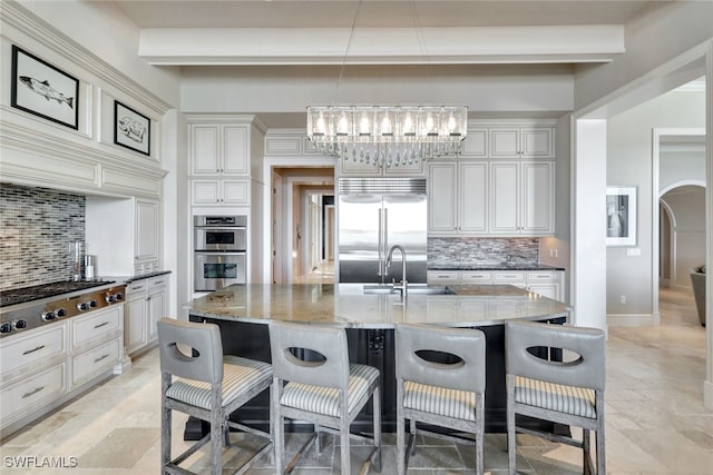 kitchen with pendant lighting, a breakfast bar, a kitchen island with sink, decorative backsplash, and stainless steel appliances