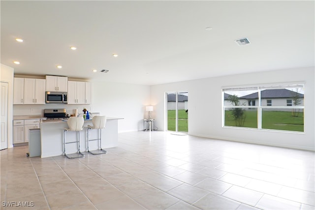 kitchen with stainless steel appliances, an island with sink, white cabinetry, a breakfast bar area, and light tile patterned flooring