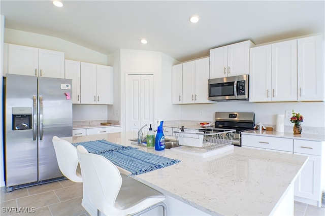 kitchen featuring white cabinets, lofted ceiling, stainless steel appliances, and an island with sink