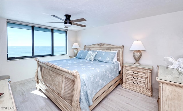 bedroom featuring ceiling fan, a water view, and light hardwood / wood-style flooring