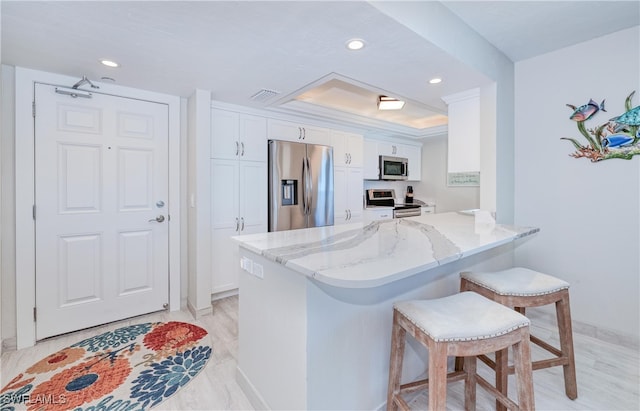 kitchen with light stone countertops, stainless steel appliances, kitchen peninsula, a kitchen bar, and white cabinets