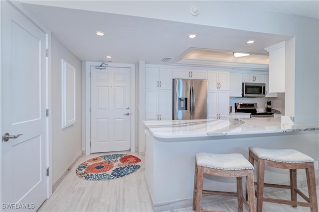 kitchen with kitchen peninsula, appliances with stainless steel finishes, a kitchen bar, and white cabinetry