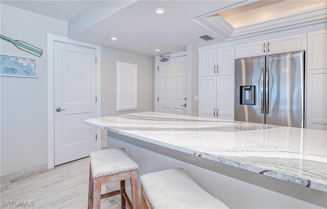 kitchen with light wood-type flooring, light stone counters, a breakfast bar, white cabinets, and stainless steel fridge with ice dispenser