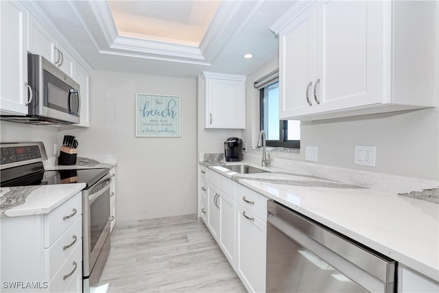 kitchen featuring stainless steel appliances, a raised ceiling, sink, light hardwood / wood-style flooring, and white cabinetry