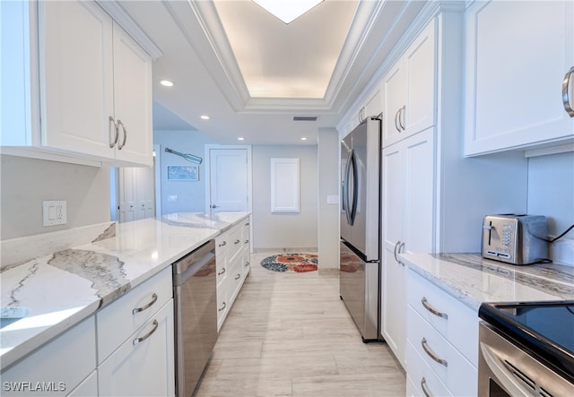 kitchen with white cabinets, light stone counters, appliances with stainless steel finishes, and a tray ceiling