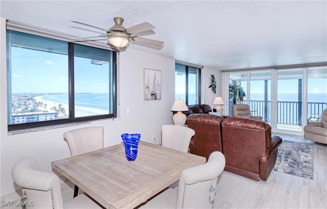 dining space with a water view, light hardwood / wood-style flooring, a wall of windows, and ceiling fan