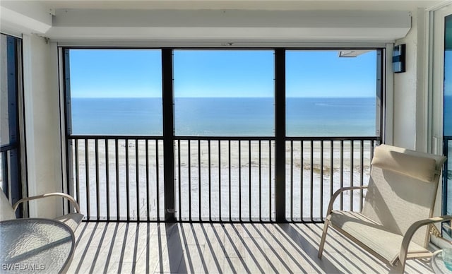 unfurnished sunroom with a water view, a healthy amount of sunlight, and a view of the beach