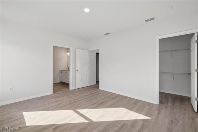 unfurnished bedroom with a spacious closet, a closet, ensuite bathroom, and light wood-type flooring