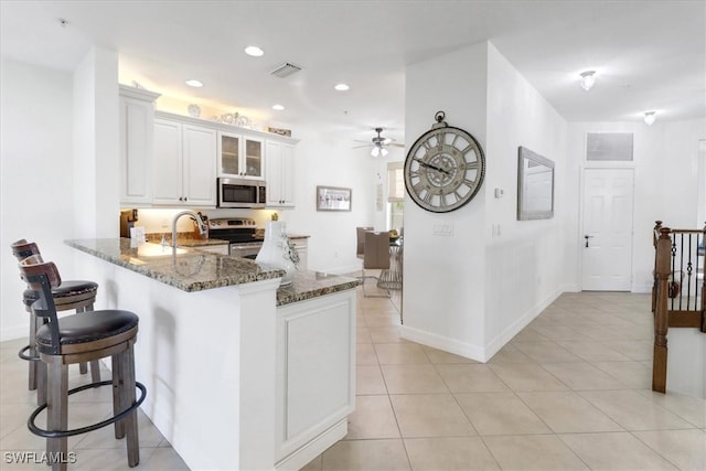 kitchen with kitchen peninsula, dark stone counters, stainless steel appliances, ceiling fan, and white cabinetry