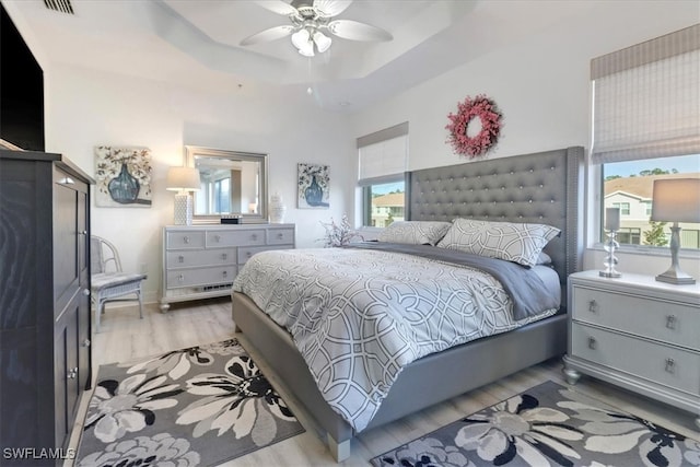 bedroom featuring a raised ceiling, light hardwood / wood-style flooring, multiple windows, and ceiling fan