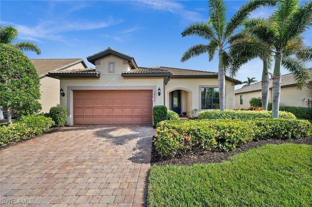 mediterranean / spanish home featuring decorative driveway, a tile roof, an attached garage, and stucco siding