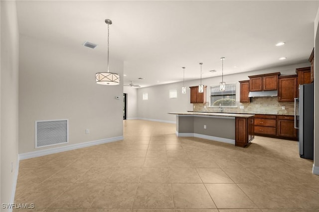 kitchen with under cabinet range hood, visible vents, open floor plan, freestanding refrigerator, and tasteful backsplash