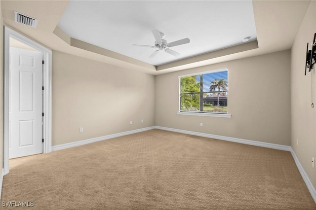 carpeted spare room featuring visible vents, a tray ceiling, ceiling fan, and baseboards