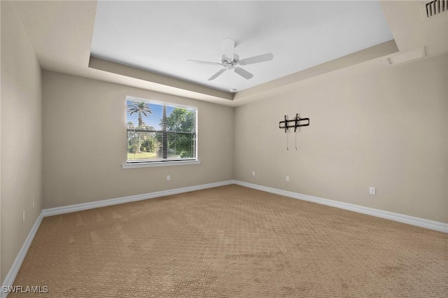 empty room with baseboards, visible vents, a tray ceiling, and carpet flooring