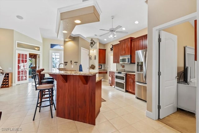 kitchen with a breakfast bar, a kitchen island with sink, light tile patterned floors, light stone countertops, and stainless steel appliances