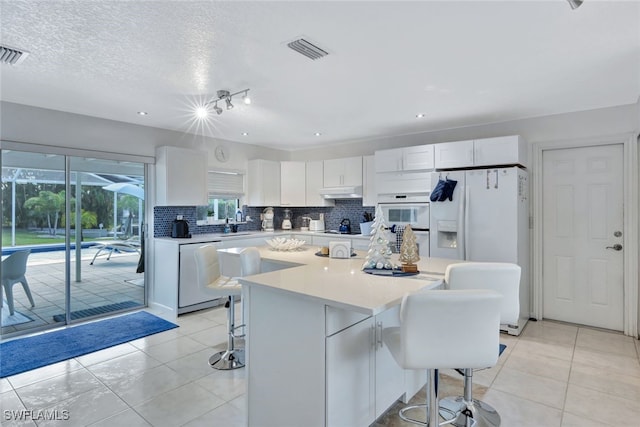 kitchen with white appliances, a center island, white cabinets, and a breakfast bar area