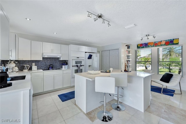 kitchen with decorative backsplash, white appliances, a center island, white cabinetry, and light tile patterned flooring