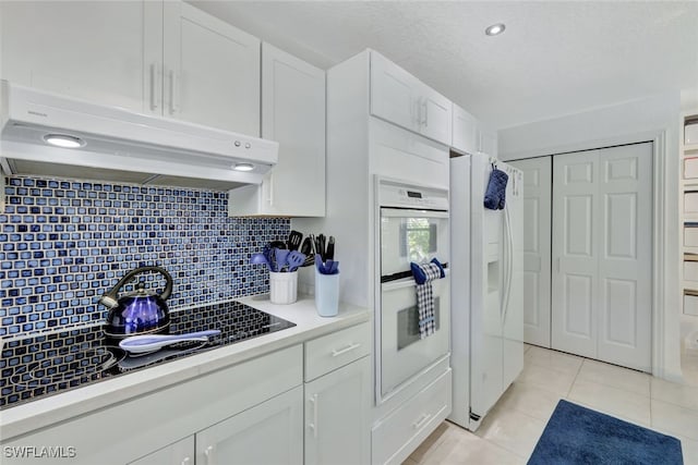 kitchen with white cabinets, white appliances, light tile patterned floors, and tasteful backsplash